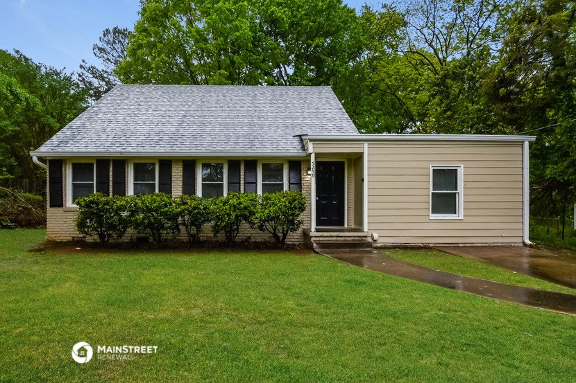 a small tan house with a green lawn and trees