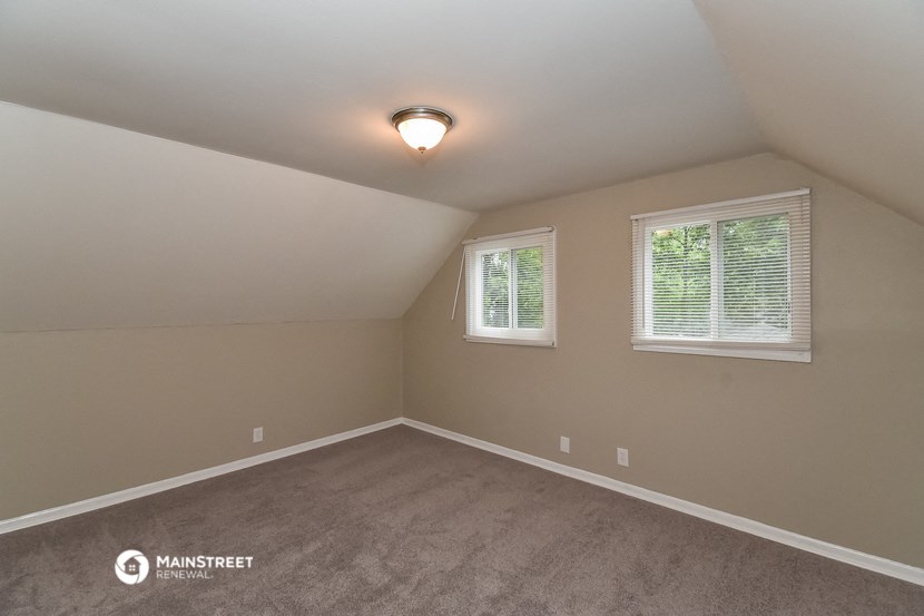 the bedroom of a house with carpet and two windows