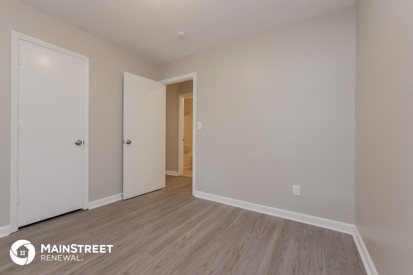 a bedroom with white walls and wood flooring and a door to the bathroom