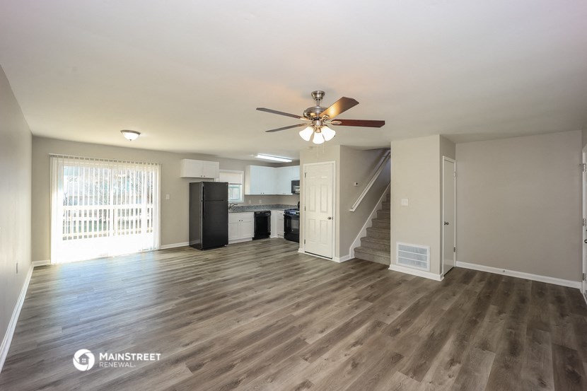 an empty living room with a ceiling fan and a kitchen