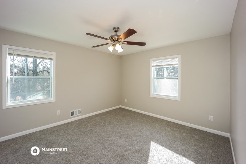 an empty room with a ceiling fan and two windows