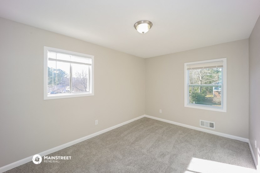 an empty bedroom with two windows and a carpeted floor