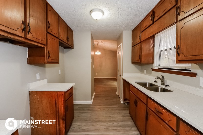 a kitchen with wooden cabinets and white counter tops and a long hallway with a sink