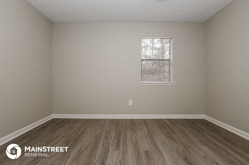 the spacious living room with wood flooring and a window