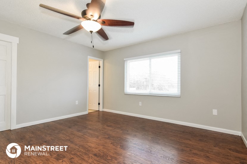the spacious living room with wood flooring and a ceiling fan