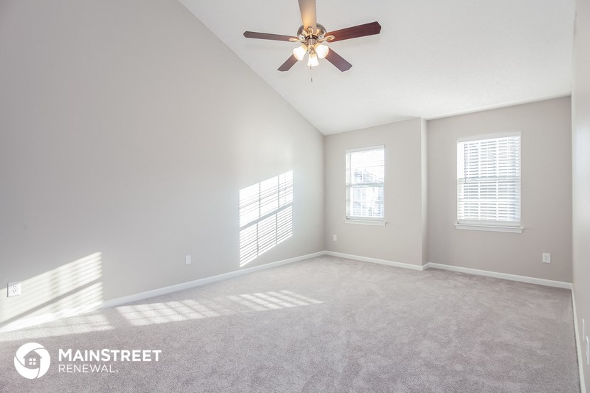 the spacious living room with ceiling fan and carpeting