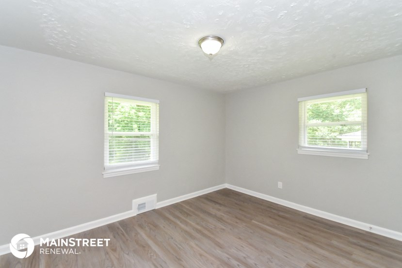 the interior of an empty room with wood flooring and two windows