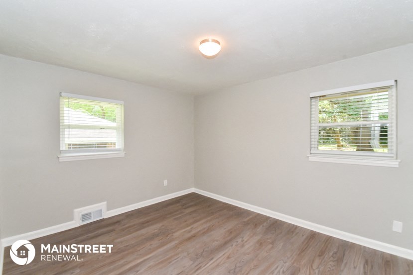 the interior of an empty room with wood flooring and two windows