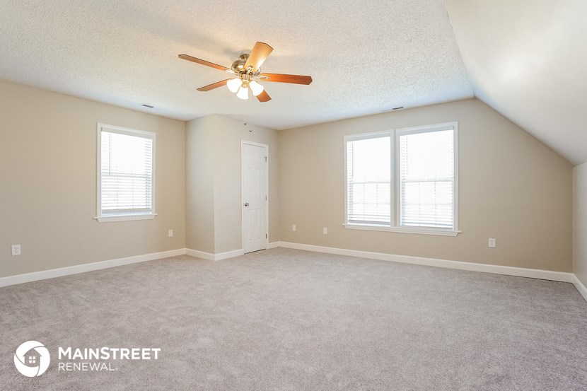 an empty living room with a ceiling fan and two windows