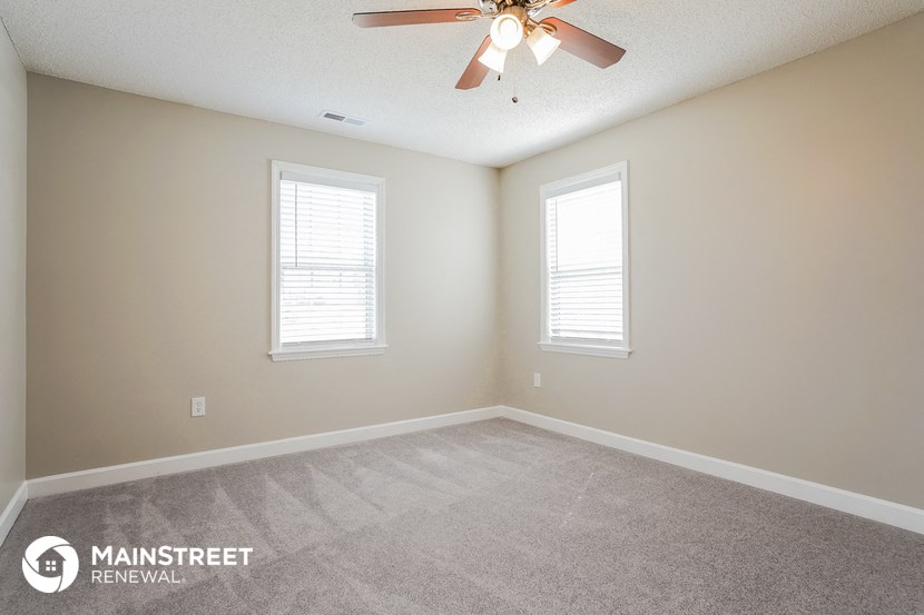 an empty room with a ceiling fan and two windows