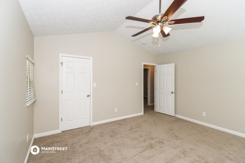 the spacious living room with two doors and a ceiling fan