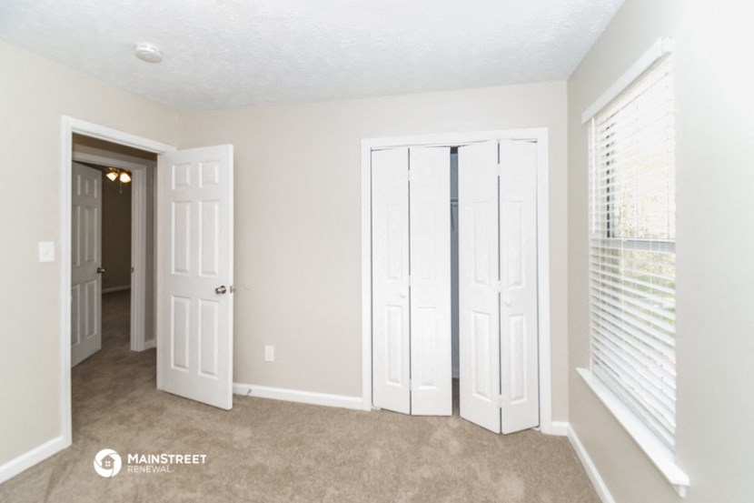 an empty living room with white doors and a hallway with a door to a closet