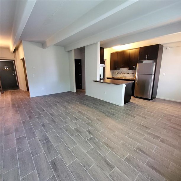 an empty living room and kitchen with a stainless steel refrigerator