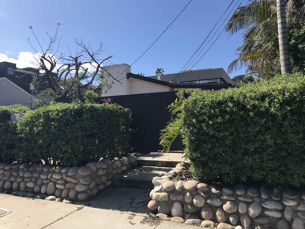 a gate with a stone wall and bushes in front of a house