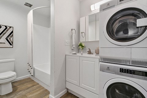 A white washing machine sits in a laundry room next to a toilet.