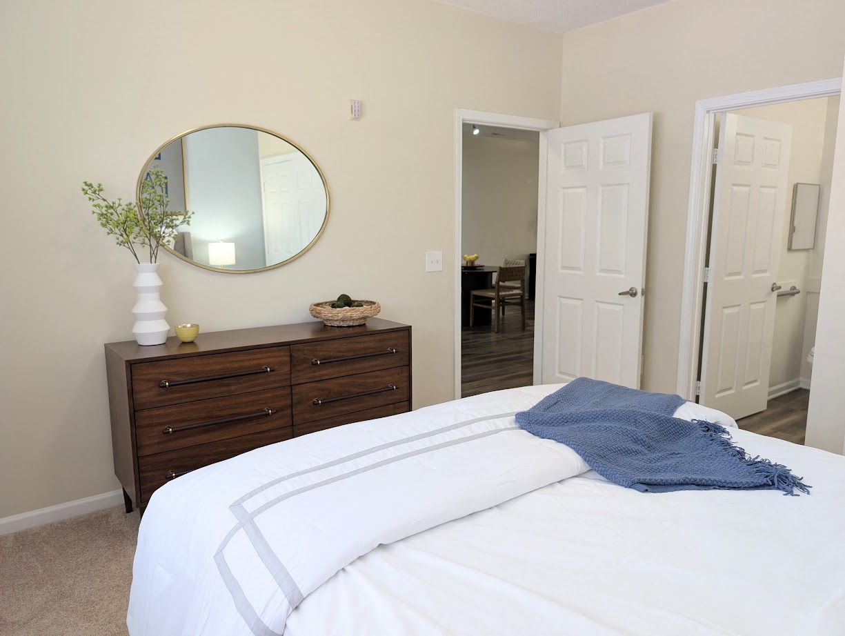 A bedroom with a white bed and a round mirror above a dresser.