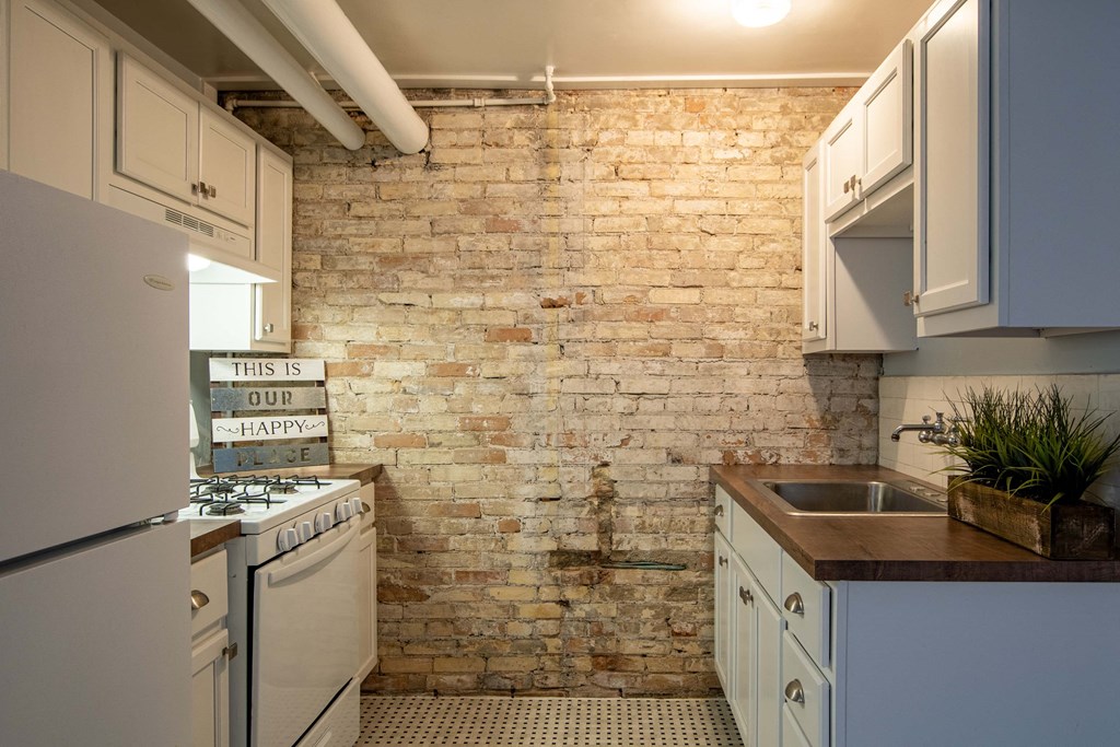 a kitchen with white cabinets and a brick wall