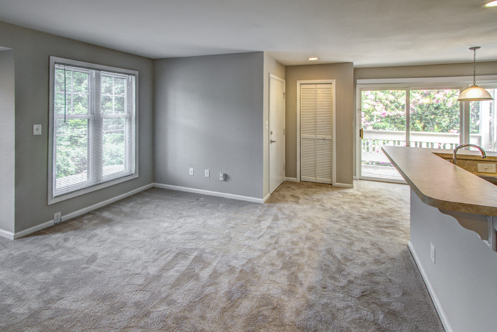 an empty living room with a kitchen and a door to a balcony