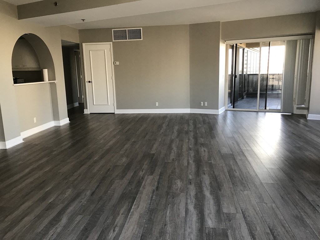 an empty living room with wooden floors and a door to a hallway