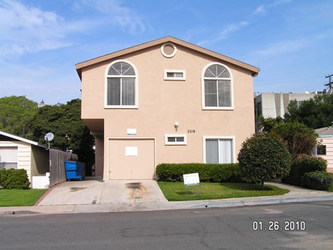 A beige house with a blue trash can in front.