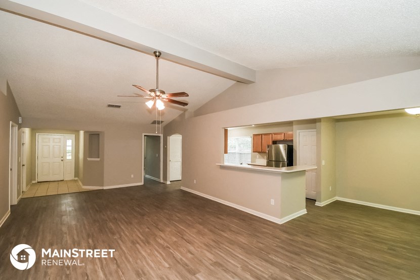 an empty living room with a ceiling fan and a kitchen