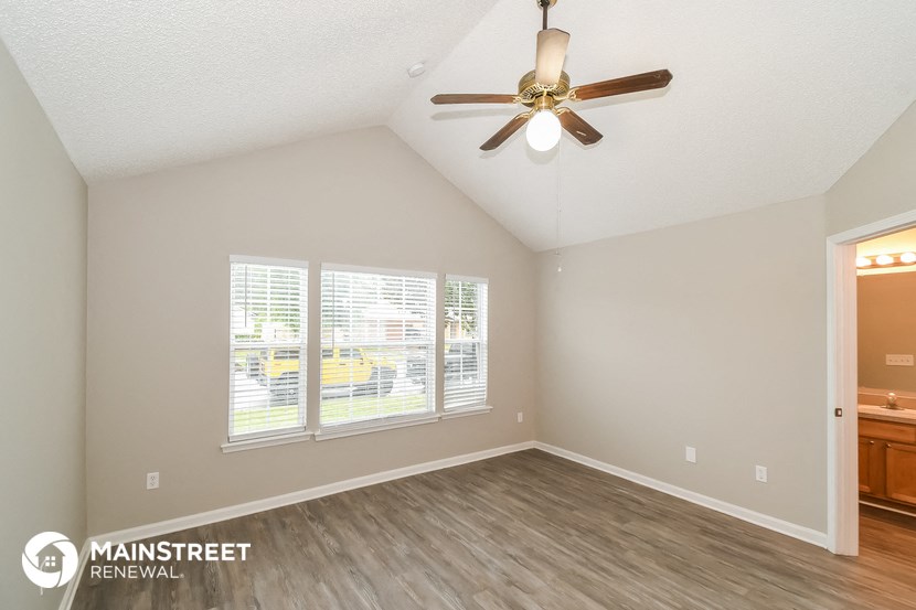 the spacious living room with ceiling fan and large windows