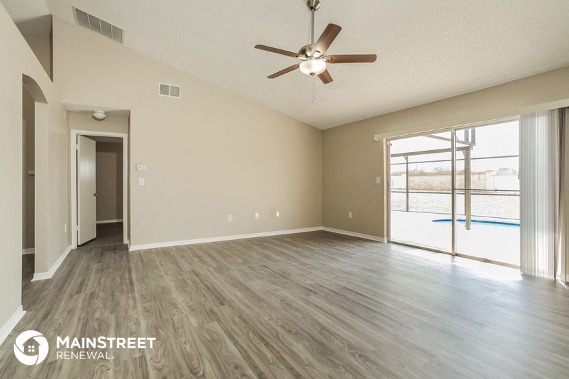 an empty living room with a ceiling fan and a door to a swimming pool