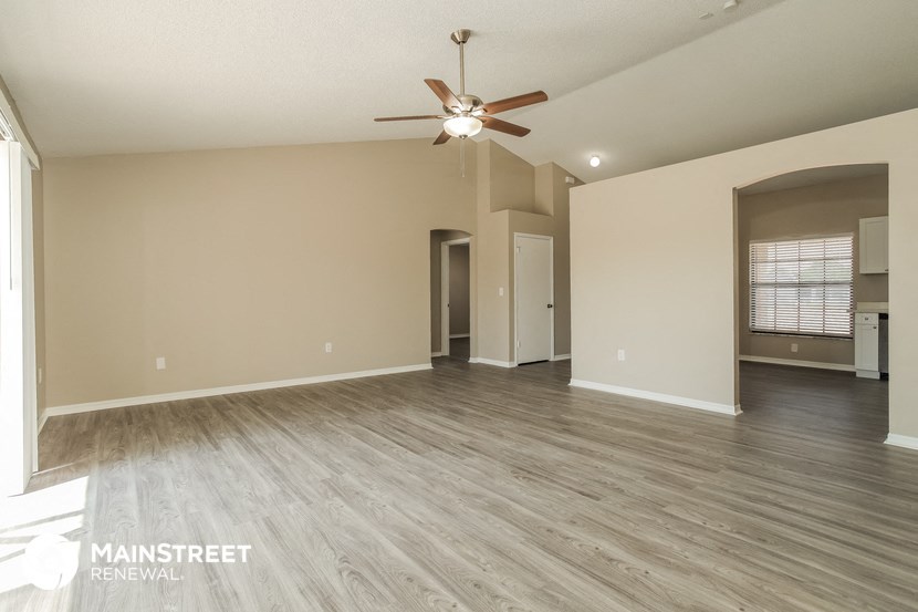 the spacious living room with hardwood flooring and a ceiling fan