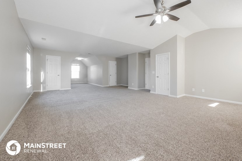 the spacious living room with ceiling fan and carpeting