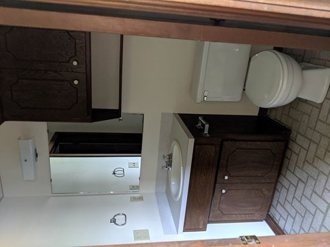 A white toilet is in a small bathroom with a wooden cabinet.