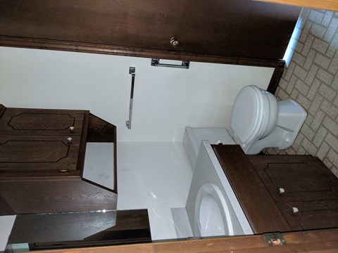 A white toilet is installed under a wooden cabinet.