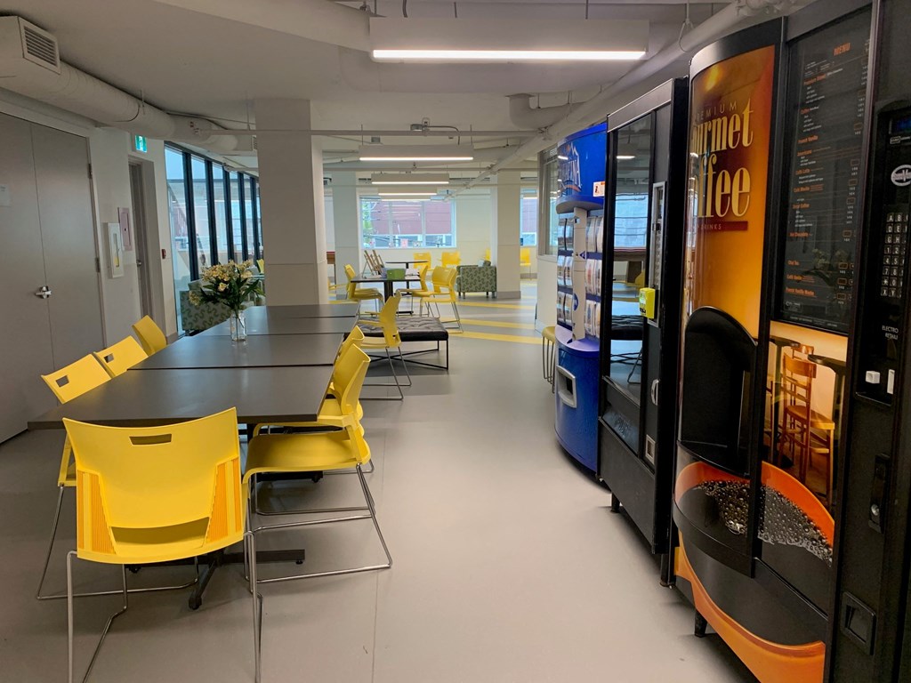 a cafeteria with yellow chairs and tables and vending machines