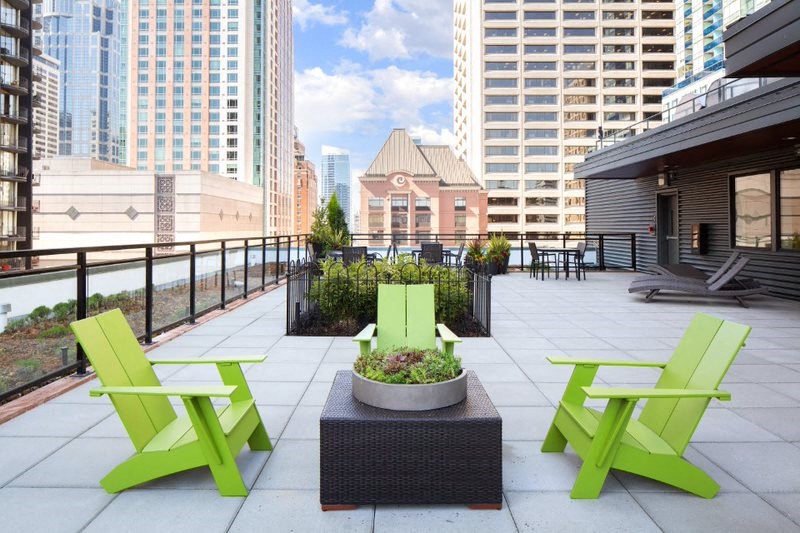 a rooftop patio with two green chairs and a planter with plants