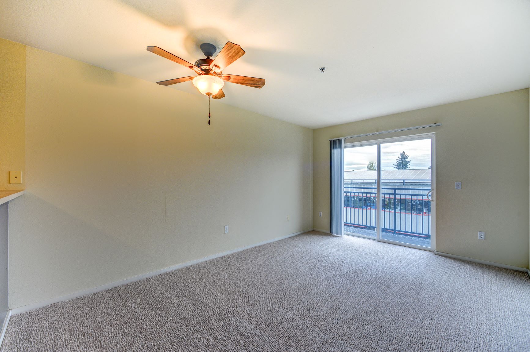 an empty living room with a ceiling fan and a door to a balcony