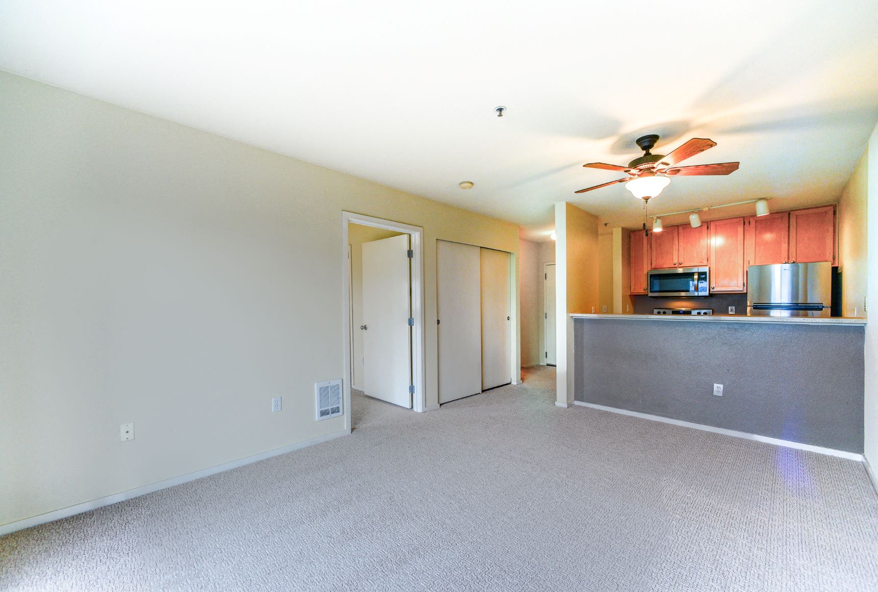 a empty living room with a kitchen and a ceiling fan