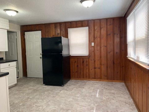 A black refrigerator sits in a kitchen with wooden walls and a white door.
