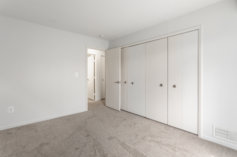 a bedroom with white cabinets and carpet and a door to a closet