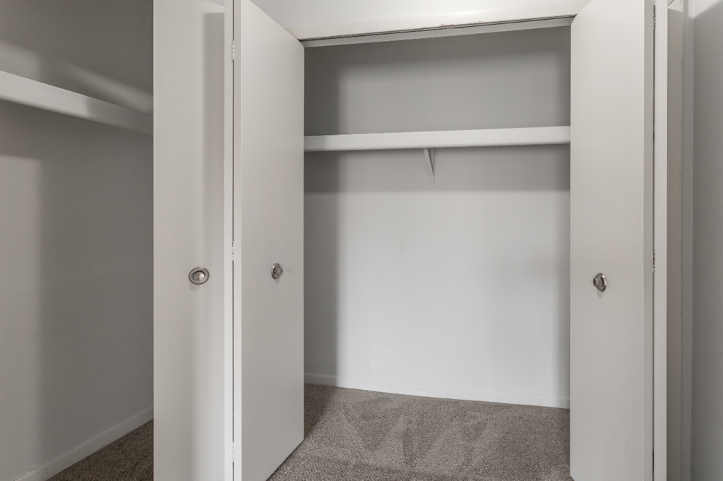 an empty closet in a home with white walls and grey carpet