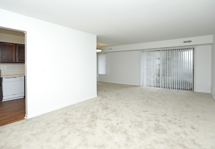 an empty living room with a white carpet and a door to a kitchen