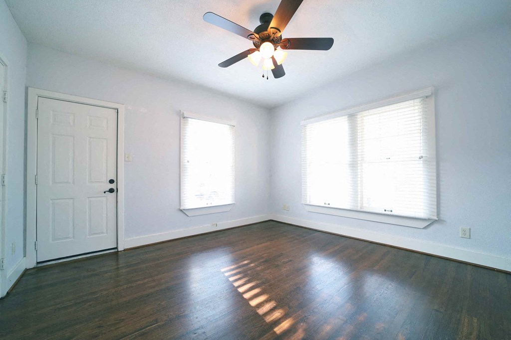 an empty living room with a ceiling fan and two windows