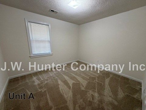 A room with a carpeted floor and a window with blinds.