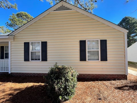 A small house with a white fence and a bush in front.