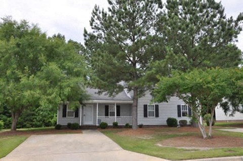 A house with a grey roof and white walls is surrounded by green trees.