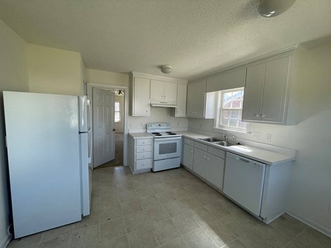 A white kitchen with a refrigerator, microwave, sink, and cabinets.