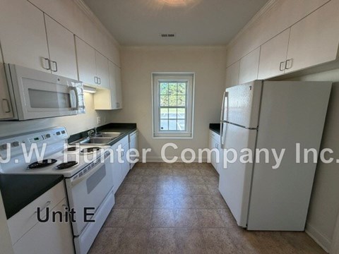 A kitchen with white appliances and cabinets is labeled J.W. Hunter Company Inc. Unit E.
