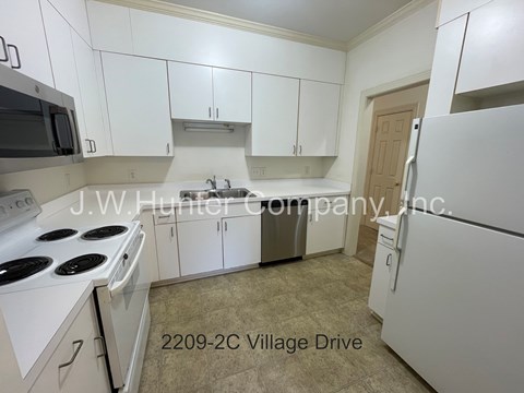 A kitchen with white cabinets and appliances, including a stove and refrigerator, with a sign that reads "J.W. Hunter Company, Inc." and an address of "2209-2C Village Drive