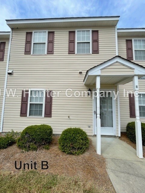 A beige house with a white door and windows with shutters.