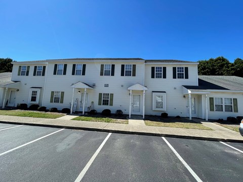 A white building with multiple windows and doors is situated in a parking lot.