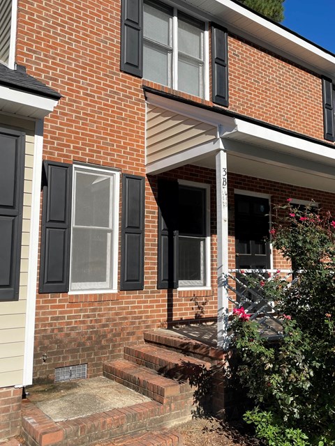 A red brick house with a white porch and black shutters.