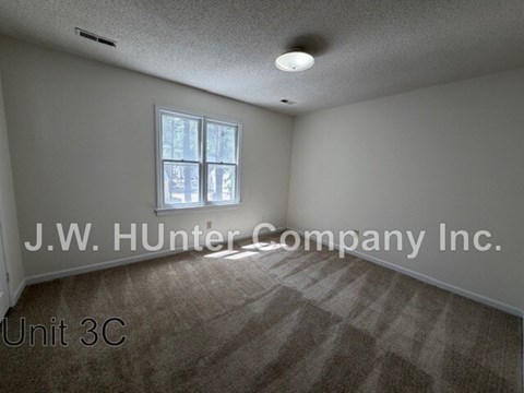 A room with a carpeted floor and a window with a view of trees.